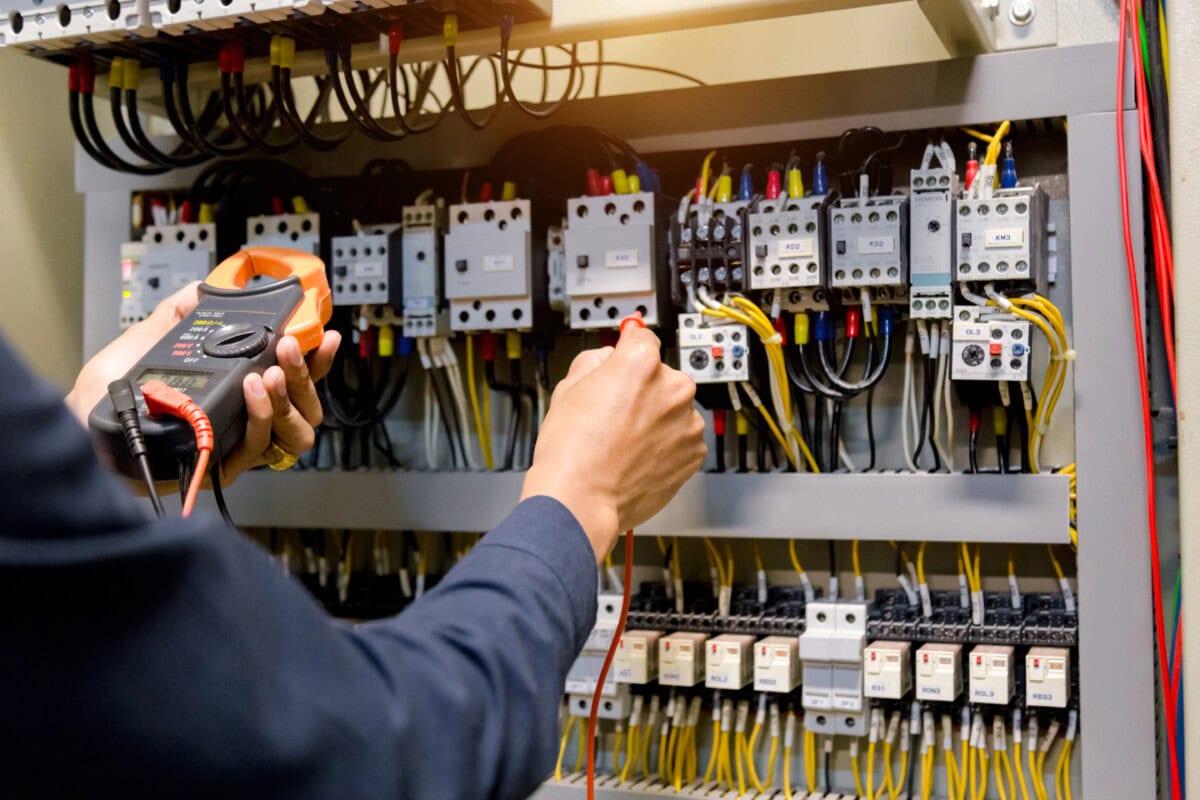 Electrician engineer work tester measuring voltage and current of power electric line in electical cabinet control.